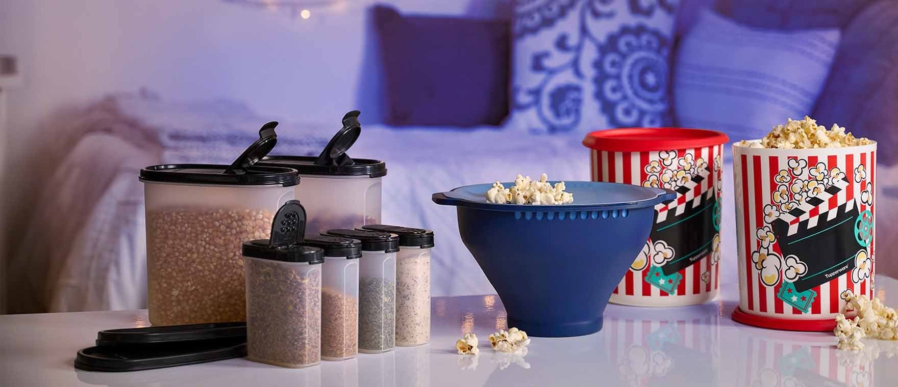 Containers of popcorn and spices on a table in front of a cozy, decorated bed.